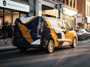 Gebrandede bezorgbus met opvallende voertuigwrap geparkeerd op drukke stedelijke straat, warme middagzon werpt lange schaduwen op het trottoir.
