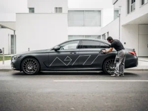 Professionele installateur strijkt donkere matte charcoal carwrap glad op luxe auto met squeegee, bewolkt daglicht, stedelijke omgeving.